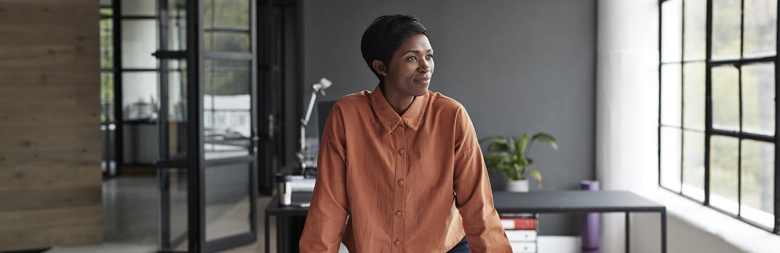 An entrepreneur stands in her office space, looking thoughtfully out a window